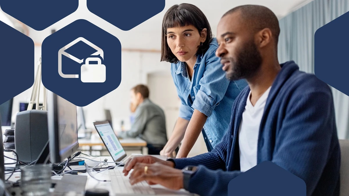 Duas pessoas trabalham em um escritório moderno, focadas em um computador. Em primeiro plano, um homem com barba curta digita no teclado, enquanto uma mulher ao seu lado se inclina levemente para observar a tela, com expressão atenta. Ao fundo, há outro profissional trabalhando em uma mesa. Elementos gráficos em formato de hexágonos aparecem sobrepostos à imagem, incluindo um ícone de chapéu de formatura com um cadeado, sugerindo tema relacionado à educação ou segurança digital.